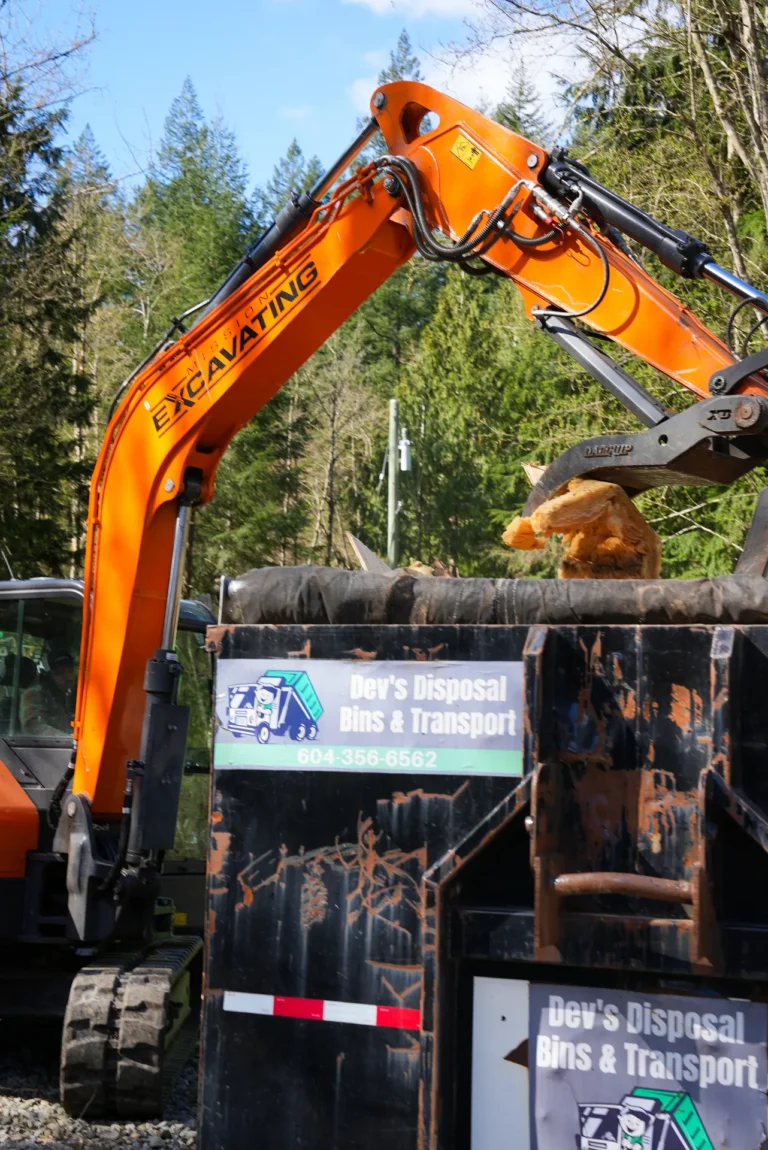 Excavator loading cleared material into a roll-off bin during land clearing in the Fraser Valley, Maple Ridge BC